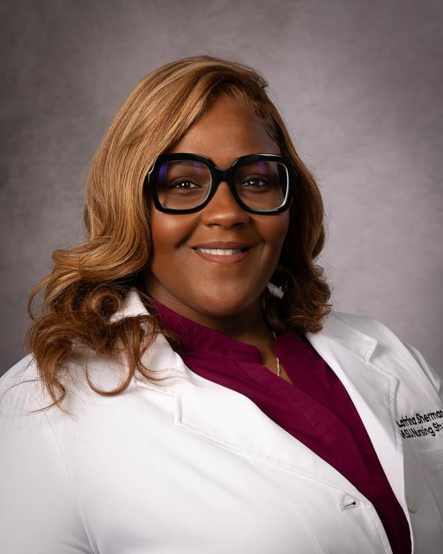 Portrait of Mississippi State University Nursing student Latrina Sherman with long hair wearing black rim glasses and a white nursing lab coat.