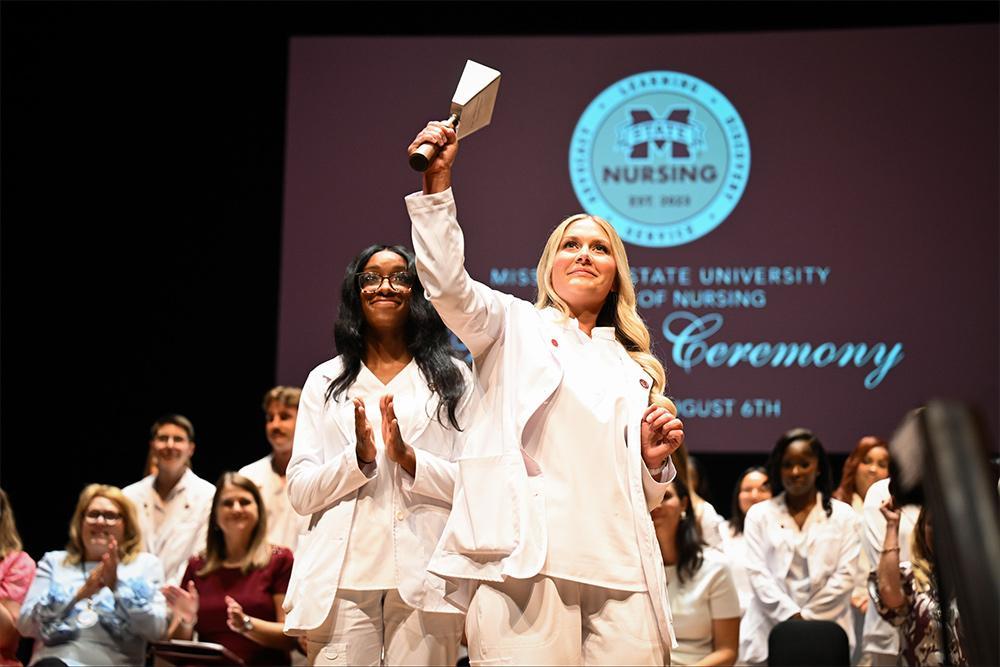 MSU Master of Science in Nursing graduate Alden Tomlinson, right, of Corinth, rings an MSU cowbell as part of a new MSN graduation tradition while Eunique Ford of Mulberry, Florida, and other graduates look on with encouragement for the incoming cohort of 52 new students who observed graduation from an upper balcony at the MSU Riley Center. (Photo by Grace Cockrell)